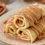 Cinnamon roll protein crepes with cinnamon sugar and creamy drizzle on a plate