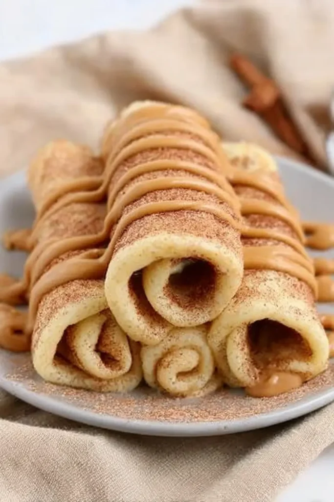 Cinnamon Roll Protein Crepes stacked with cinnamon sugar and creamy drizzle