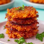 Crispy sweet potato hash browns stacked on a plate with fresh herbs