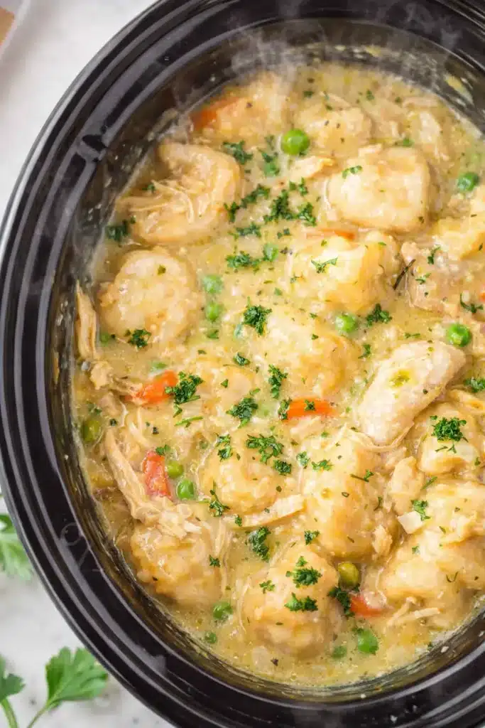 Crockpot chicken and dumplings with creamy broth, fluffy dumplings, peas and carrots