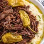 Crockpot Mississippi pot roast with shredded beef and peppers over mashed potatoes
