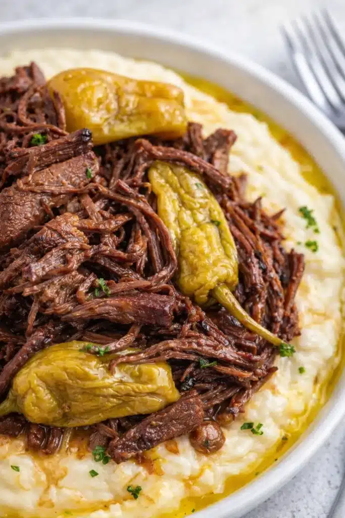 Crockpot Mississippi pot roast with shredded beef and peppers over mashed potatoes