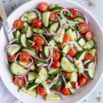 Fresh cucumber tomato salad with red onion and herbs in a bowl