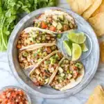 Easy chicken tacos with avocado, pico de gallo, and lime on a plate with tortilla chips
