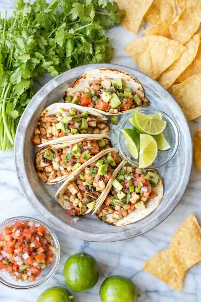 Easy chicken tacos with avocado, pico de gallo, and lime on a plate with tortilla chips
