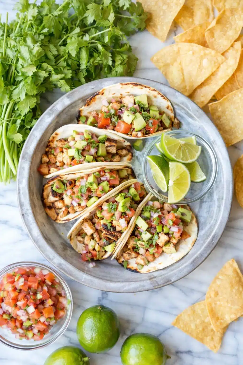 Easy chicken tacos with avocado, pico de gallo, and lime on a plate with tortilla chips