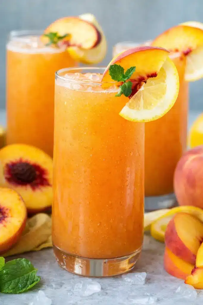 Peach lemonade in glass with ice, peach slices, lemon, and mint garnish