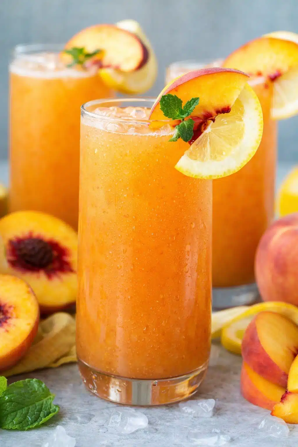 Peach lemonade in glass with ice, peach slices, lemon, and mint garnish