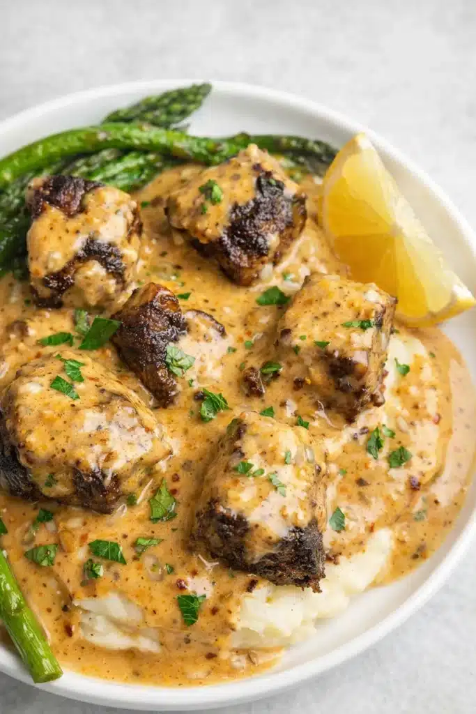 Garlic butter steak bites with creamy sauce over mashed potatoes and greens