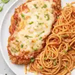 Healthy baked chicken parmesan with spaghetti and melted cheese on a plate