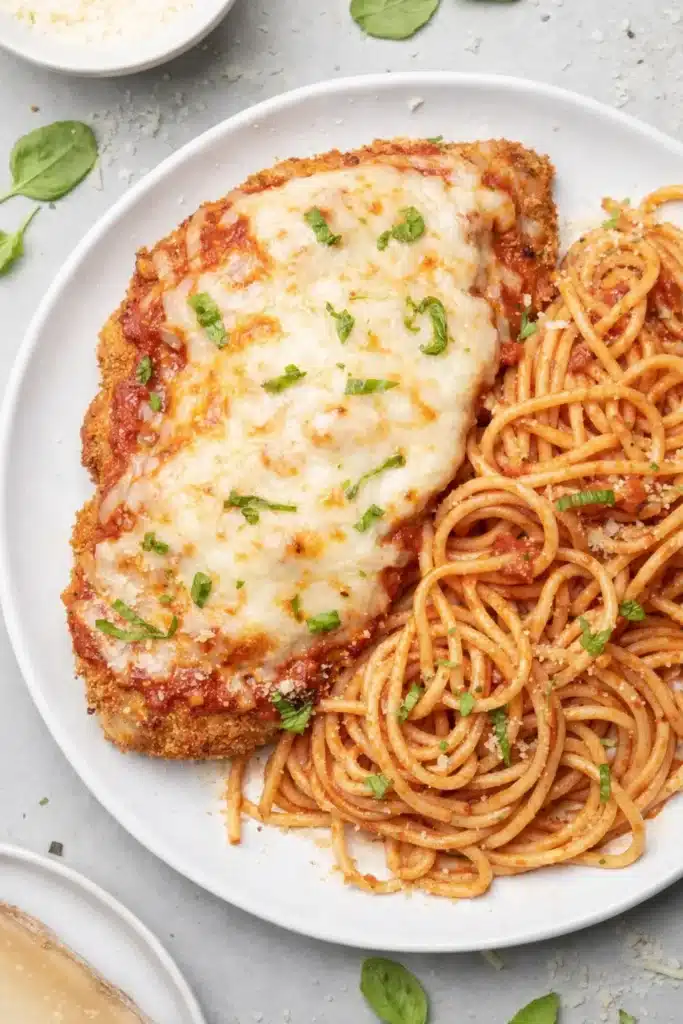 Healthy baked chicken parmesan with spaghetti and melted cheese on a plate