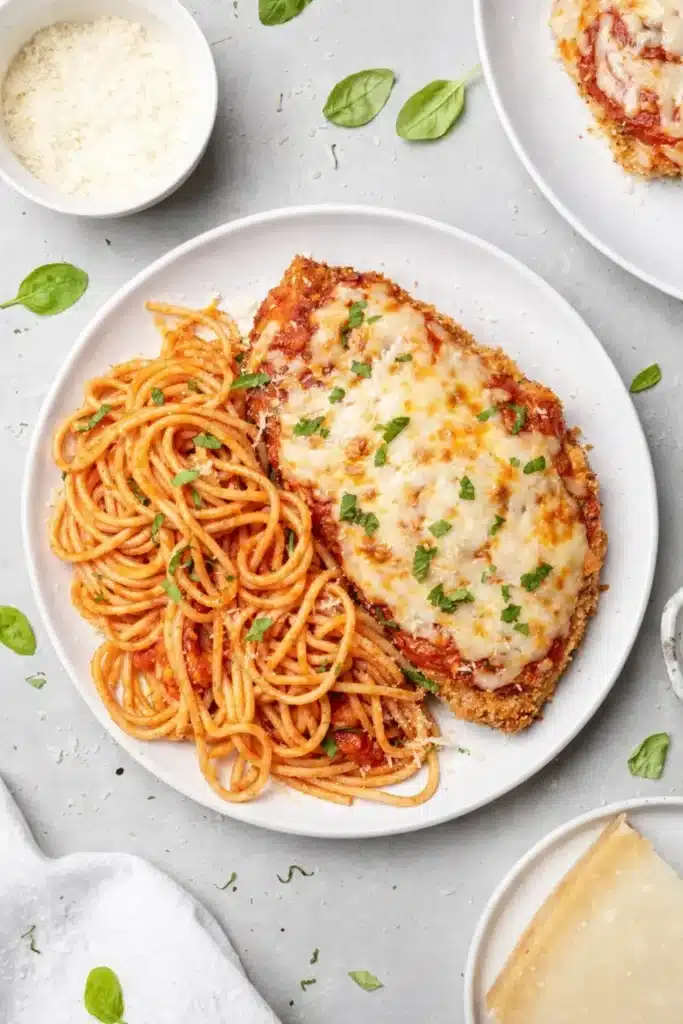 Healthy Baked Chicken Parmesan with spaghetti and fresh basil on a plate
