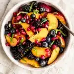 Honey lime basil peach fruit salad with berries and pomegranate in a bowl