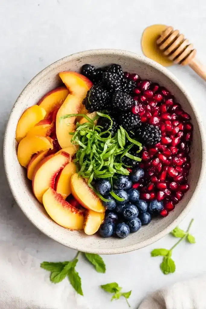 Honey Lime Basil Peach Fruit Salad with fresh peaches, berries, and basil in a bowl