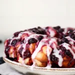 Lemon blueberry monkey bread with glaze and fresh berries on a plate