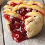 Mini cherry pie with flaky crust and glossy cherry filling on a rustic surface