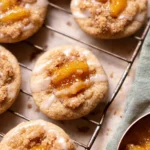 Peach cobbler cookies with jam center, crumble topping, and glaze on cooling rack