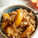 Peach crisp with oat topping served warm in a bowl with soft baked peaches