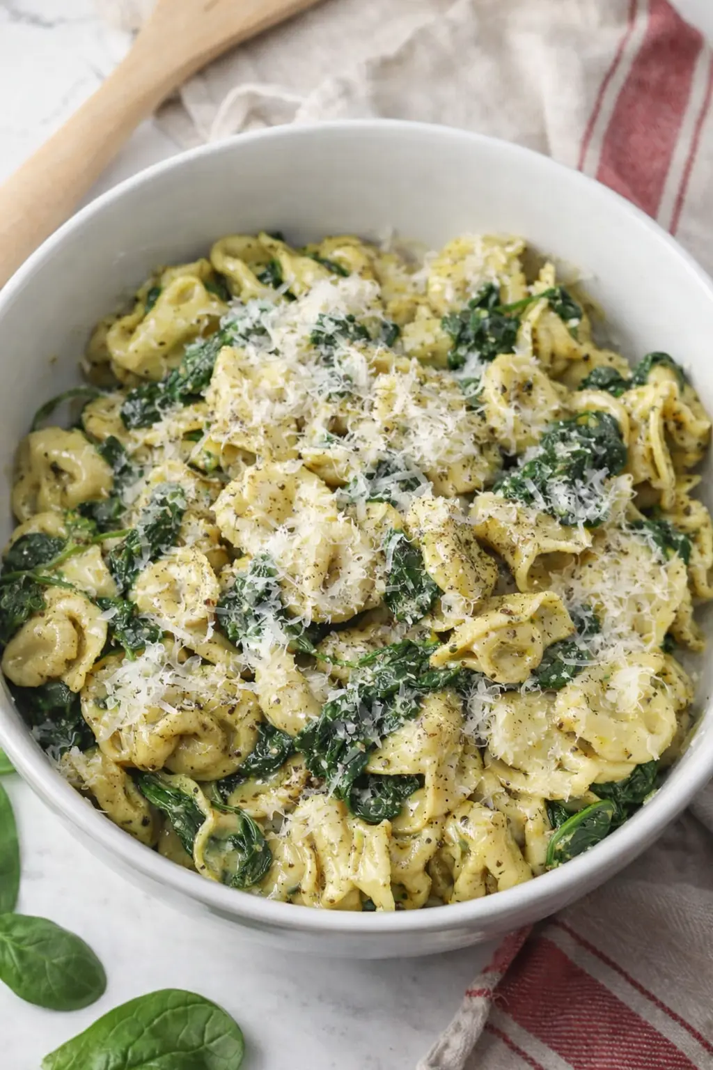 Pesto tortellini with spinach and parmesan in a white bowl