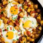 Potato and egg hash with crispy potatoes, sunny eggs, and herbs in a skillet