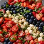 Red white and blue caprese salad with strawberries blueberries mozzarella and basil in bowl
