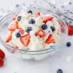 Red white and blue cheesecake salad with strawberries blueberries and marshmallows in a bowl
