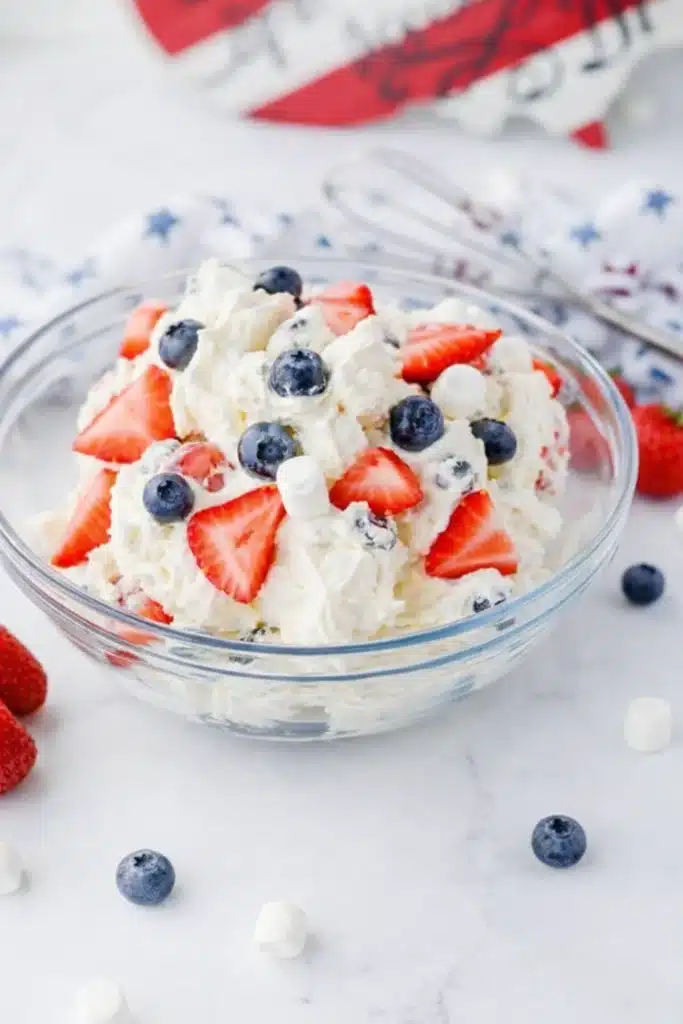 Red white and blue cheesecake salad with strawberries blueberries and marshmallows in a bowl