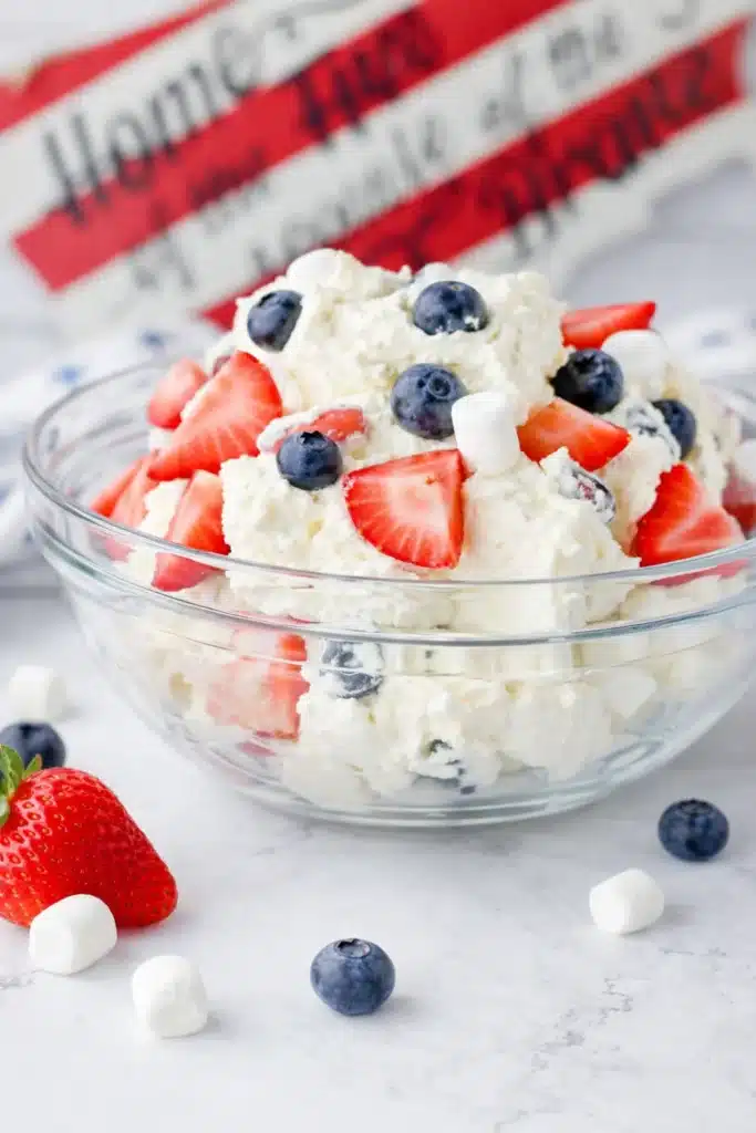 Red White and Blue Cheesecake Salad with strawberries blueberries and marshmallows in glass bowl