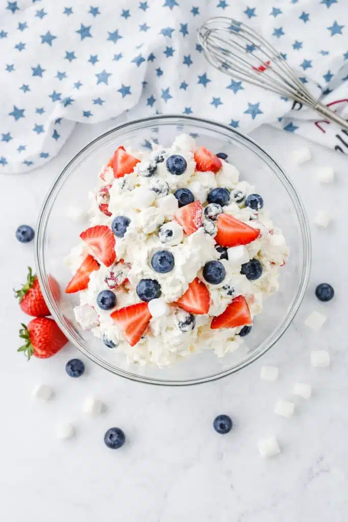 Red White and Blue Cheesecake Salad in bowl with strawberries blueberries and marshmallows