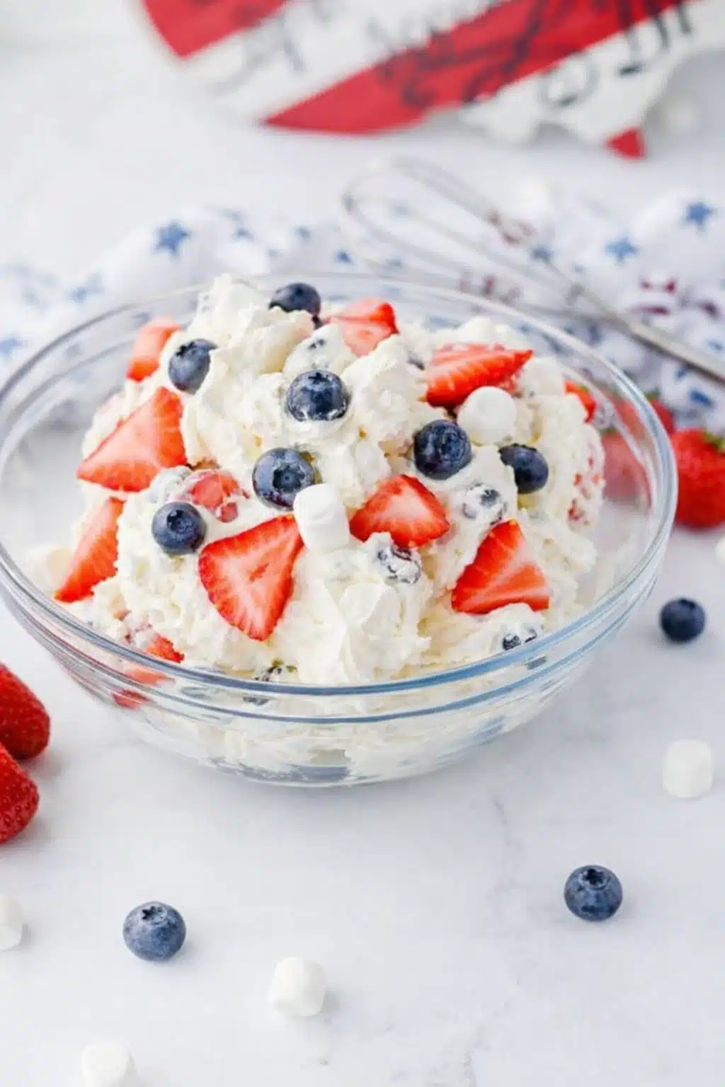 Red white and blue cheesecake salad with strawberries blueberries and marshmallows in a bowl