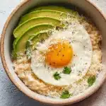 Simple savory avocado oatmeal with fried egg and cheese in a ceramic bowl