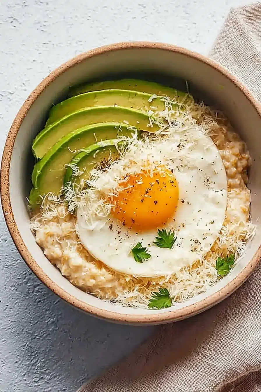 Simple savory avocado oatmeal with fried egg and cheese in a ceramic bowl