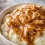 Slow cooker chicken and gravy over creamy mashed potatoes in a bowl