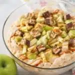 Snickers apple salad with caramel drizzle and green apples in a creamy dessert bowl