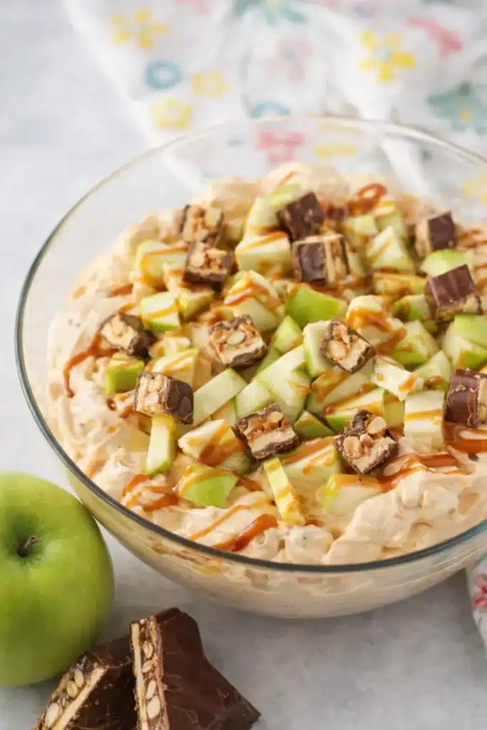 Snickers apple salad with caramel drizzle and green apples in a creamy dessert bowl