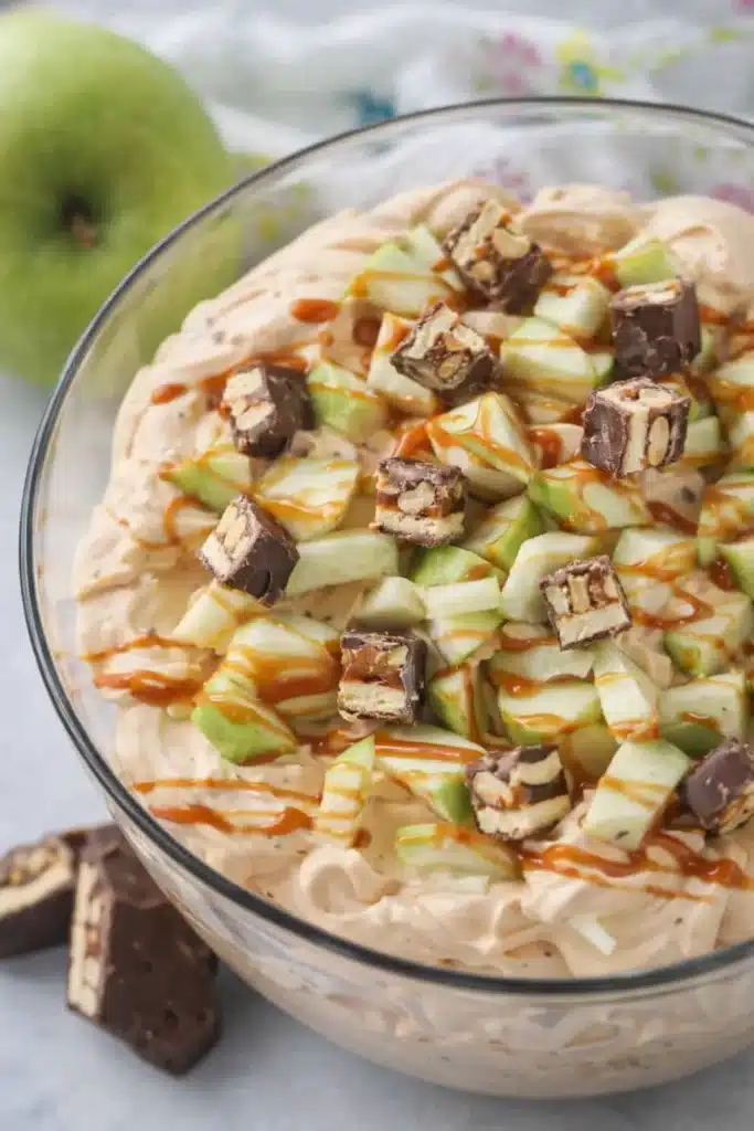Snickers apple salad with caramel drizzle, chopped apples, and candy pieces in a creamy dessert bowl