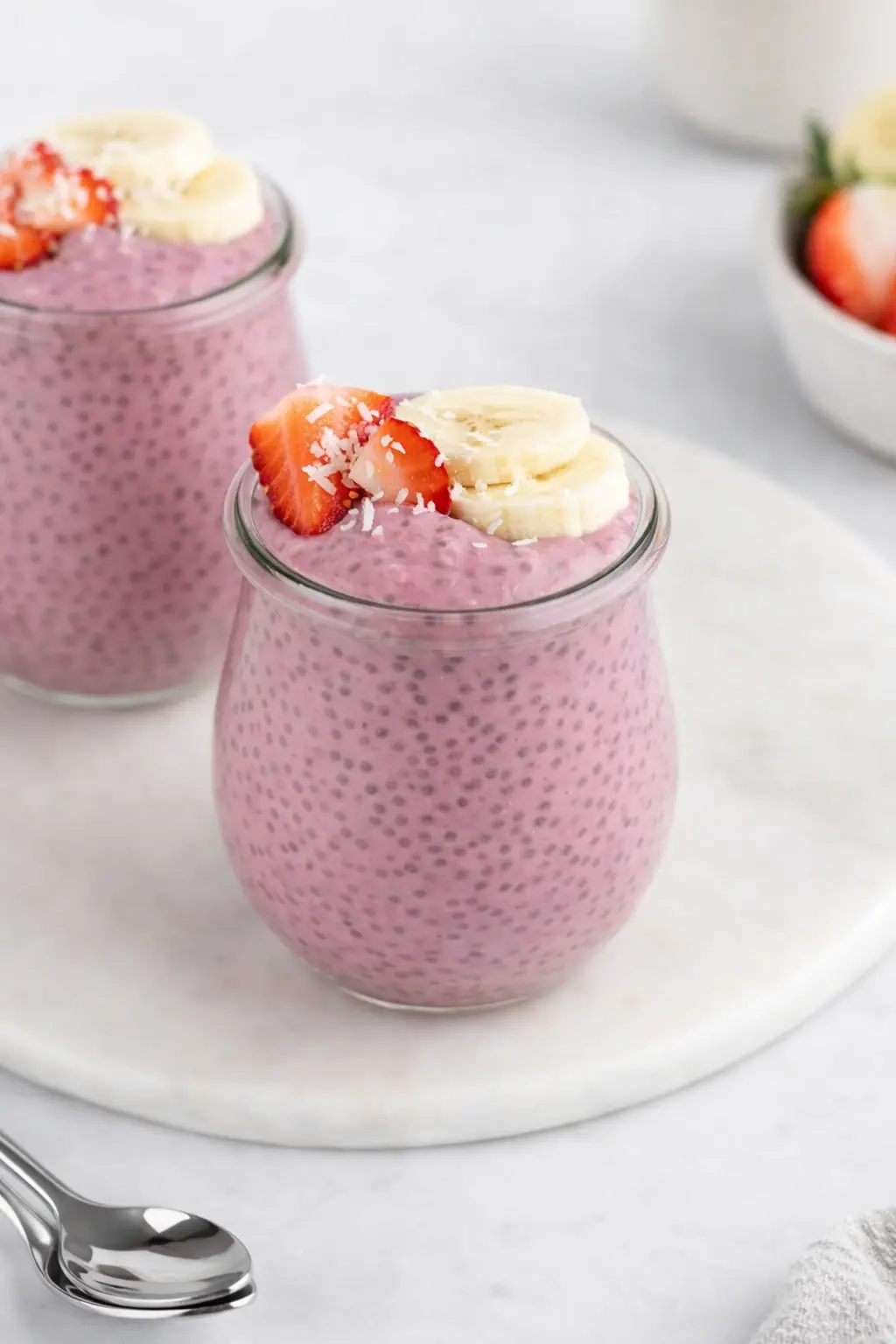 Strawberry banana chia pudding in jars topped with fresh fruit and coconut flakes