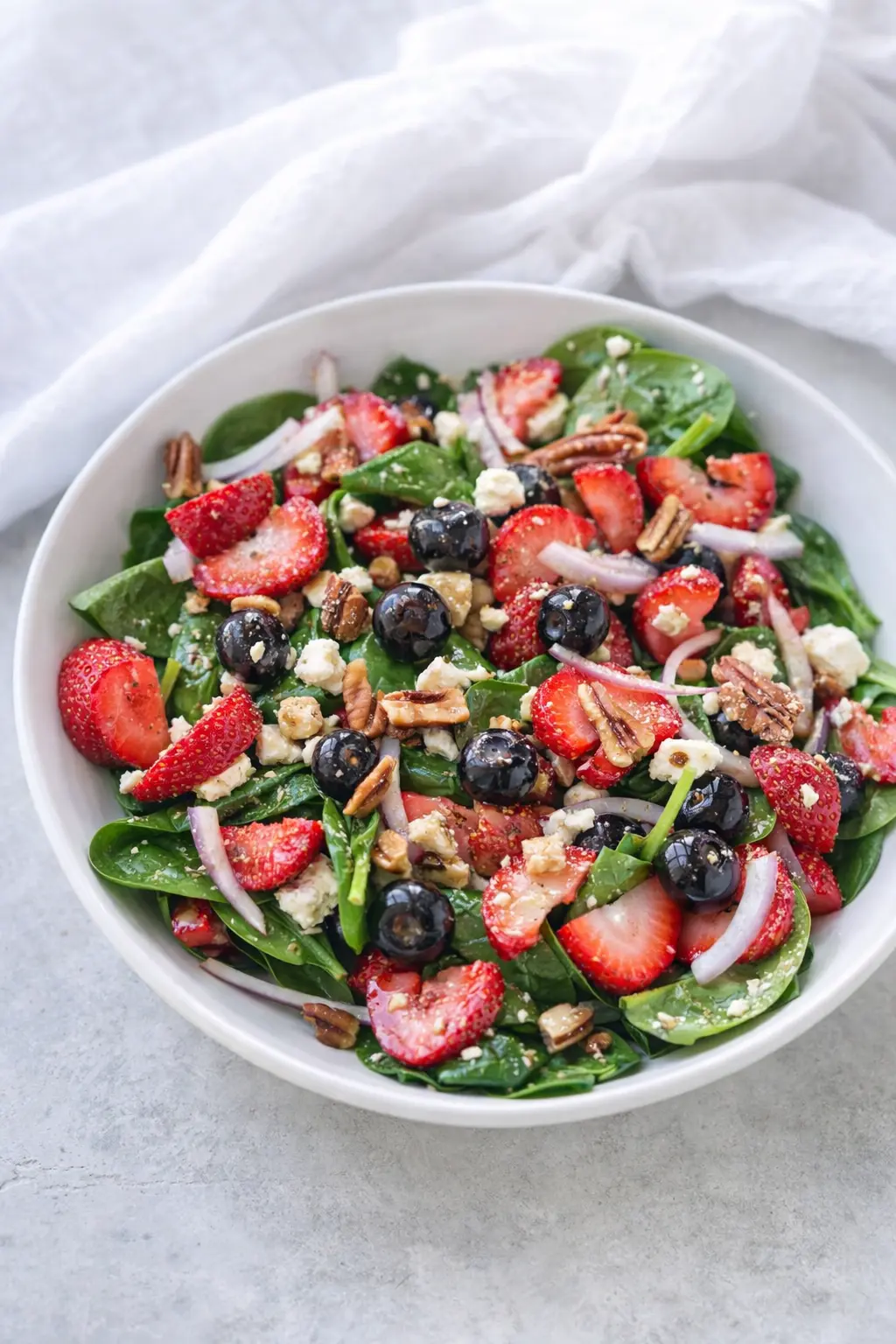 Strawberry spinach salad with feta, blueberries, pecans, and balsamic dressing in a white bowl