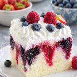 Summer berry poke cake slice with whipped cream and fresh strawberries blueberries