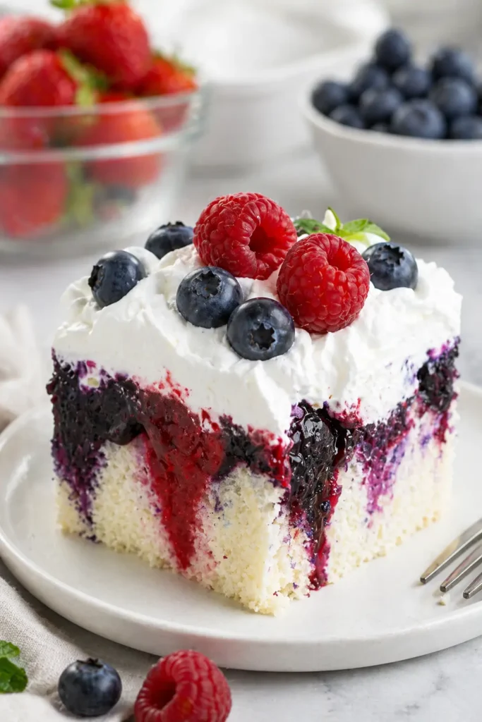 Summer Berry Poke Cake slice with whipped cream and fresh berries
