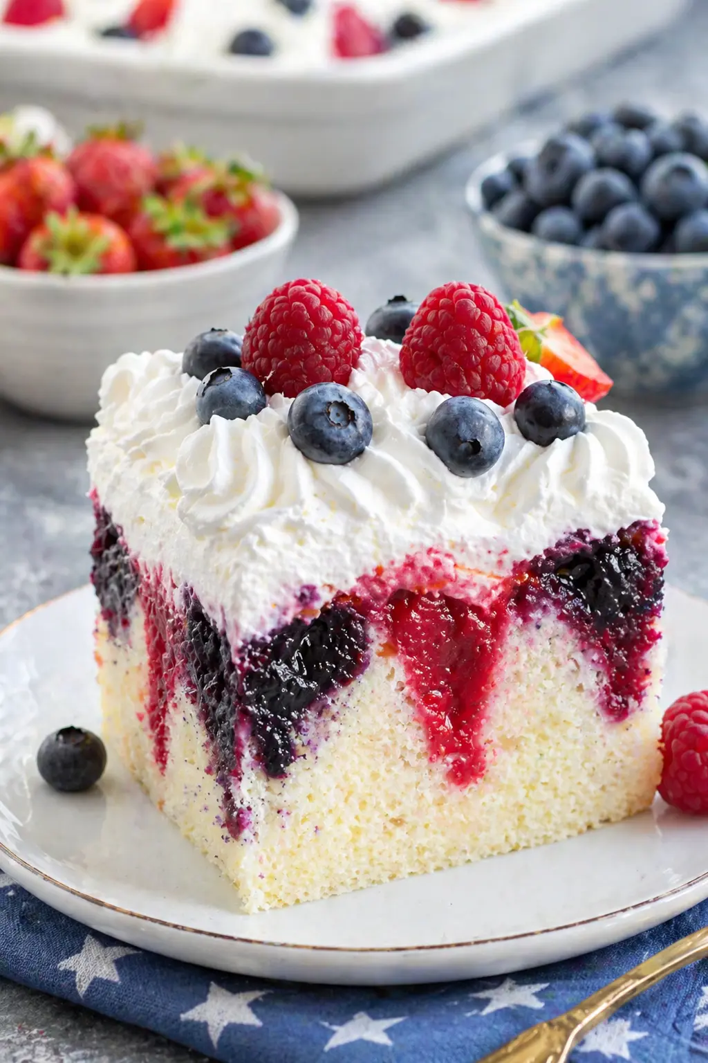 Summer berry poke cake slice with whipped cream and fresh strawberries blueberries