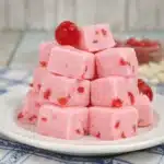 White chocolate cherry fudge cubes stacked on a plate with glossy cherry topping