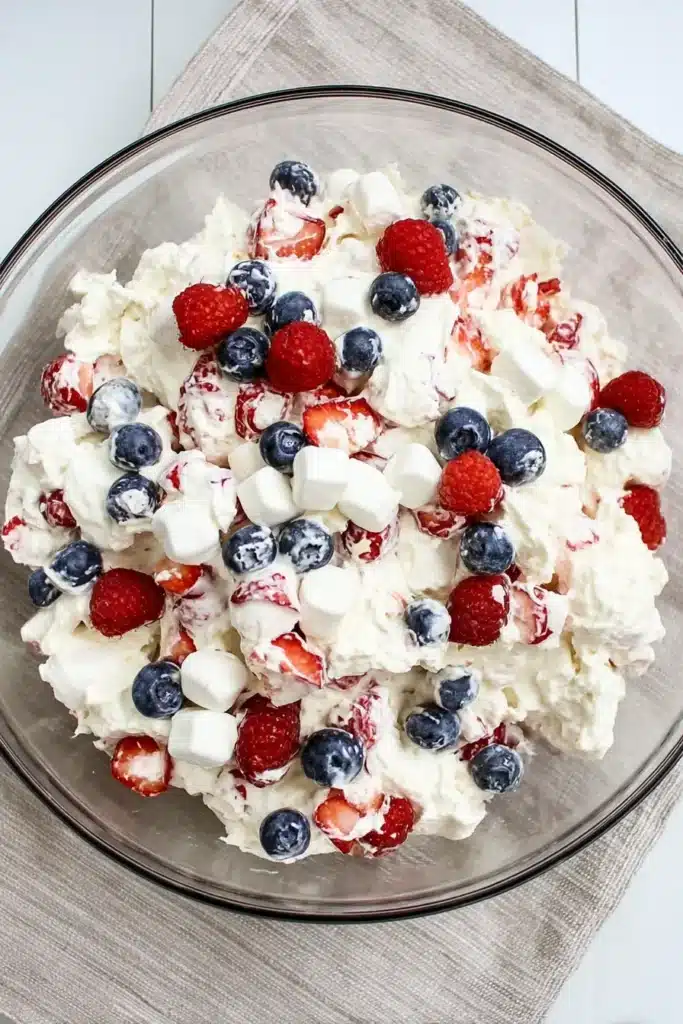 Red White and Blue Cheesecake Salad in a glass bowl with fresh berries