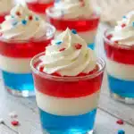 4th of July jello shots with red white and blue layers topped with whipped cream and sprinkles