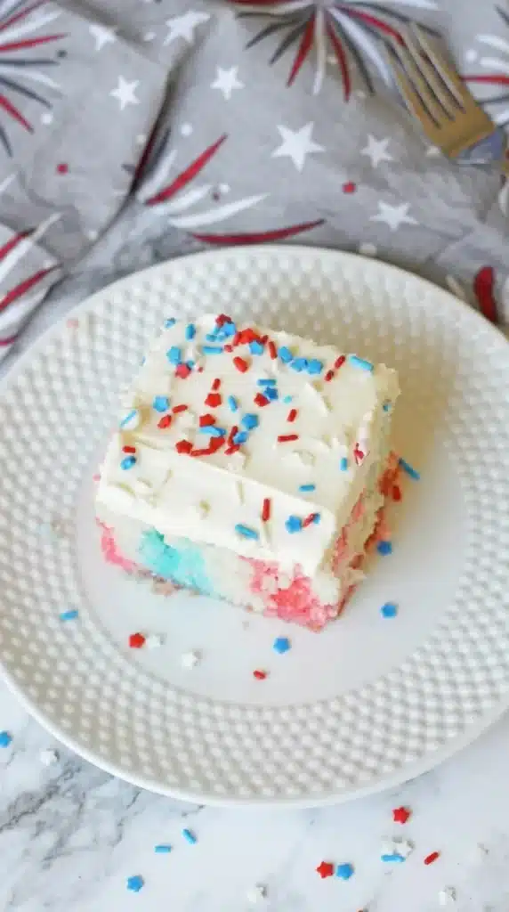 4th Of July Poke Cake Recipe slice with red and blue gelatin and creamy frosting