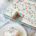 Close up 4th Of July Poke Cake Recipe slice with patriotic sprinkles and creamy frosting