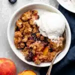 Blueberry peach crumble with vanilla ice cream and buttery oat topping in a rustic bowl