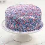 Fireworks Cake covered in patriotic red white and blue sprinkles on a cake stand