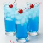 Blue Fourth of July cocktail with cherries and ice in tall glasses on a rustic summer table