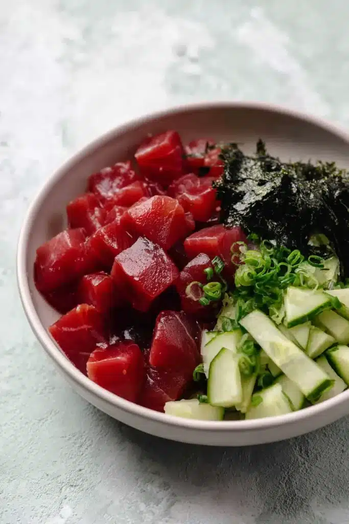  Ahi tuna poke bowl ingredients with seaweed, cucumber, and scallions in a ceramic bowl